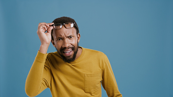 Confused, surprise and portrait of black man on blue background for news, gossip and announcement. Shock, glasses and face of person with wtf, doubt and disappointed facial expression in studio