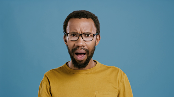 Studio, portrait and black man with shocked face for news, announcement or reaction for discount. Surprise, frown and emoji of confused person with gossip, secret or drama on blue background