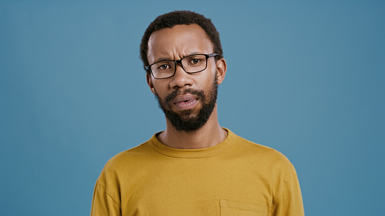 African, man and studio with disappointment, disagreement and opinion with frustration. Model, face and portrait with glasses, annoyed and upset for decision with failure isolated on blue background