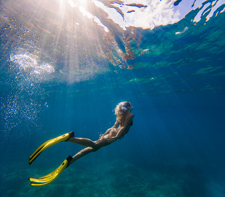 Young woman diving underwater, she's wearing red bikini and mask and diving flipper. Sun makes beautiful sunrays