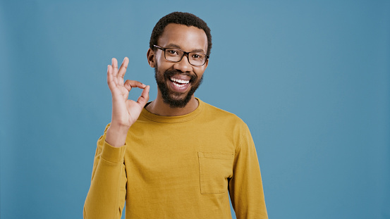 Black man, OK hand gesture and portrait with agreement, success or support for feedback on blue background. Yes, vote or review with happy model, like emoji for praise and pride with smile in studio