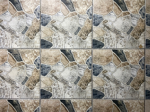 male hands lay out a square tile with a pattern in the middle of a mosaic made from large parts of tiles to create a decorative surface for furniture, the work of a tiler decorating products