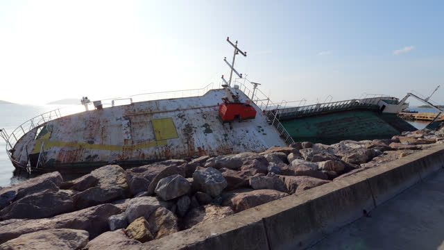 Next to stony embankment, cargo and passenger vessel lies in water on its side