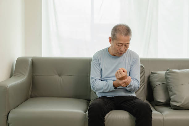 an elderly asian male patient suffers from pain and numbness in his hand from rheumatoid arthritis. elderly man massaging hand with pain in wrist health problems concept - arthritis senior adult rheumatoid arthritis sadness ストックフォトと画像