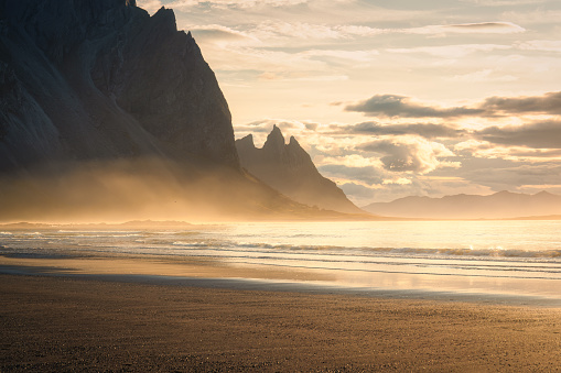 Breathtaking view of golden sunrise shines with wave spray on Vestrahorn mountain during summer at Stokksnes peninsula, Iceland