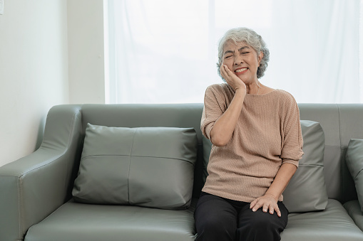 Sick elderly woman touching neck, having unhappy shoulder and neck pain, feeling severe neck pain and stressed from neck pain after sleeping badly, health and medicine concept.