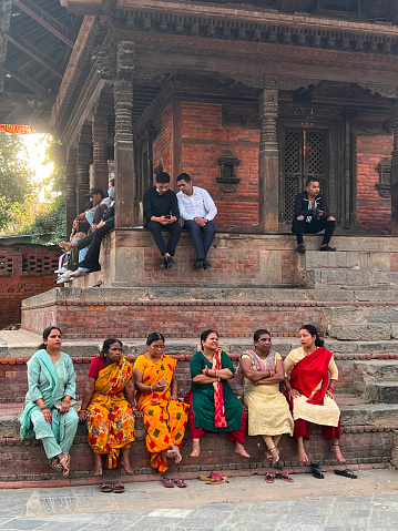 women with tradational dress are sitting infront of temple and men are background vertical still from Katmandu, Nepal, June 2023