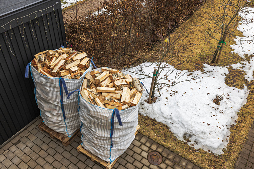 Close-up top view of spring garden with transport bags of chopped birch firewood near house. Sweden.