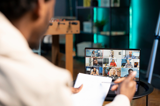 Remote employee in video conference meeting chatting with multi ethnic international team while working from home. Self employed man in online video call with coworkers in apartment