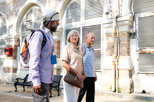 A senior Sikh tour guide on walking tour with two senior traveler along the heritage Sultan Abdul Samad Buildings, Kuala Lumpur.