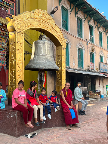 monk women and child are sitting under big bell at temple in Katmandu, Nepal, June 2023