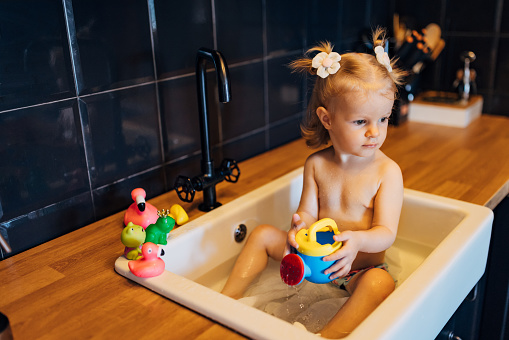 A baby girl lined up her rubber ducks on the edge of the sink while she played with other toys