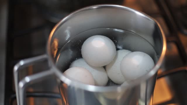 Eggs boiling in metal pan in boiling water. Close up.