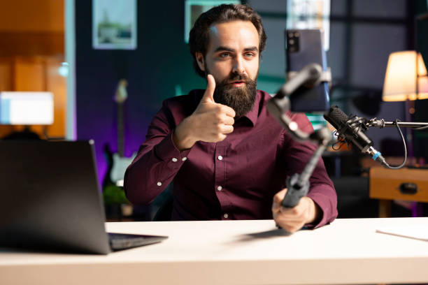 istock Content creator doing thumbs up sign, using cellphone on selfie stick to shoot video 2043207964