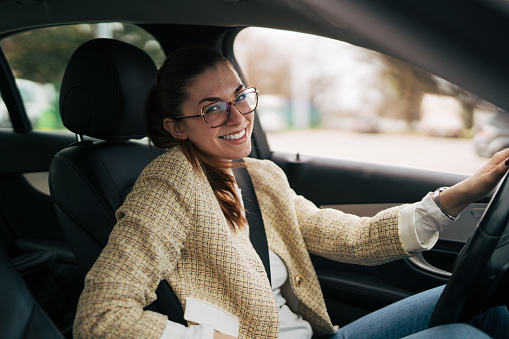 Portrait of a young business woman sitting in a car, wearing eyeglasses and looking happy. He looks at the camera.