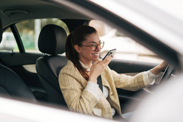 una giovane donna sorridente è seduta in macchina e sta registrando un messaggio audio. - road trip audio foto e immagini stock