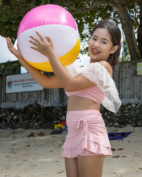 A Filipino girl playing with a beachball on a sandy beach