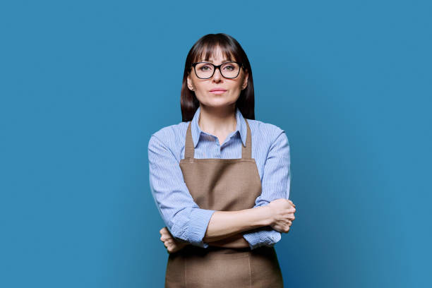 istock Confident serious middle-aged woman in apron on blue background 2043224575