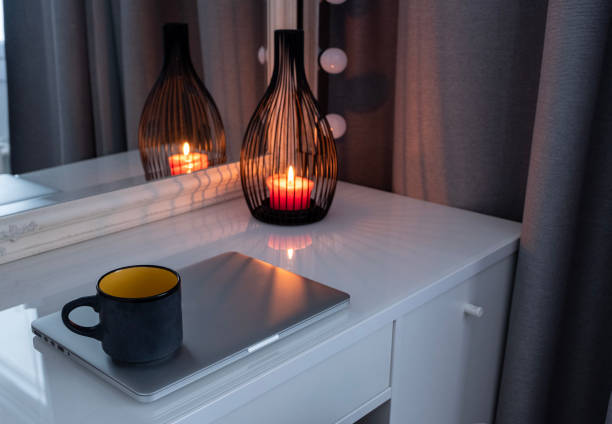 Interior, dressing table with a lamp and a lit candle. Cup of coffee and laptop.
