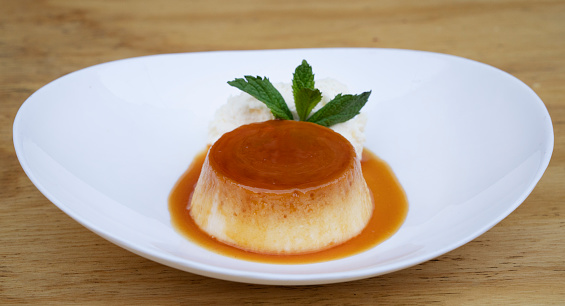 Traditional gourmet dessert. Closeup view of a flan with cream and caramel, in a white dish on the wooden table.