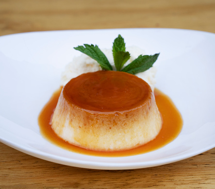 Traditional gourmet dessert. Closeup view of a flan with cream and caramel, in a white dish on the wooden table.