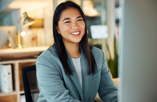 Portrait, smile and business woman in office, workplace and female person on computer in company at night for career. Face, happy advisor and entrepreneur or Asian professional working in Cambodia