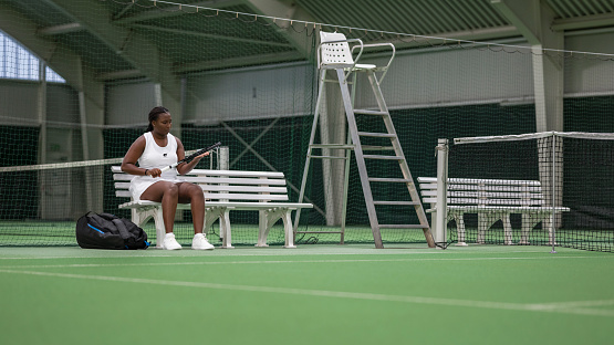 Front view female tennis player sitting on bench while holding tennis racquet in tennis court. Sport and healthy lifestyle concept.
