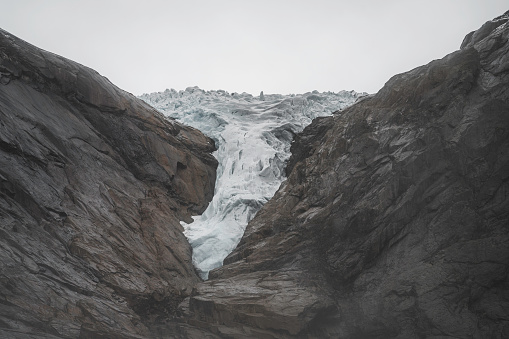 Detail of the norwegian Briksdalsbreen glacier on a mountain landscape, cloudy, with the tongue of the glacier in the center.