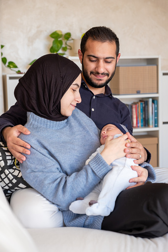 Arabic Muslim parents share a tender moment with their newborn daughter, radiating love and joy in their home.