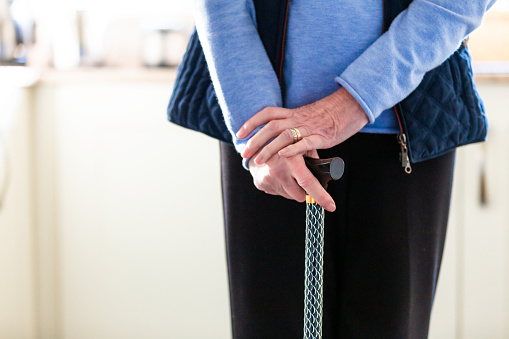 Close up of the hands of a senior woman resting on the top of her walking cane at home.