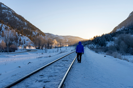 Mature man walks along train track in winter on a cold day as sun rises over distant mountains