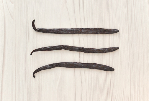 Closeup of vanilla beans from Africa on a whitewashed wood background.