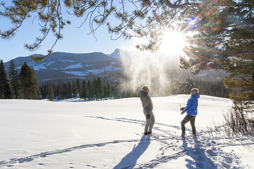 Mature couple play in snow together, mountains distant