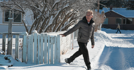 Mature man walks through gated fence in winter into back alley