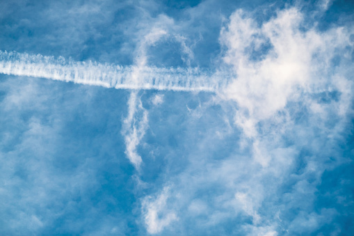 Condensation airplane trail in blue cloudy sky
