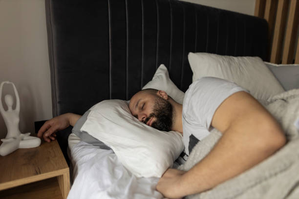 istock Apartment Bedroom: Handsome Young Man Sleeping Cozily on a Bed in His Bedroom in the morning. Comfortable Apartment with Guy Resting for Productive next Day.  stock photo 2043382009