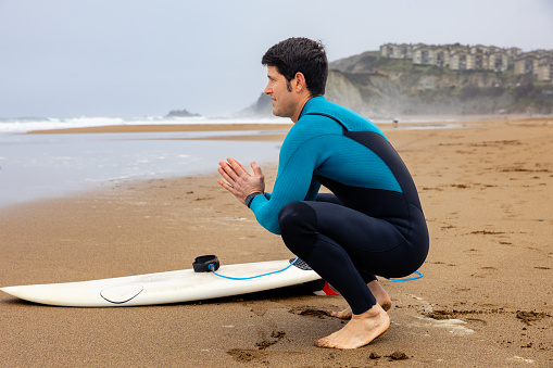 Young athlete sitting in front of the sea with elasticity before catching the waves.