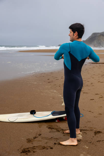 istock Young surfer on the shore stretching and warming up before catching the waves, vertical photo. 2043385110