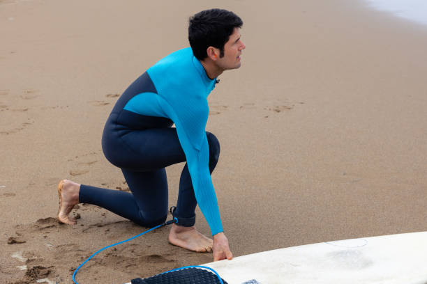 istock Young surfer on the shore tying his surfboard to his ankle, blank space. 2043385118