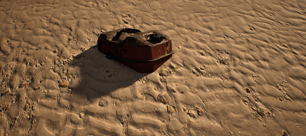 Rusty brown jerrycan lying in rippled sand of beach.