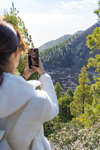 woman takes a vertical photo with her mobile phone of the dry lava on the side of a volcano in La Palma, Canary Islands, vertical