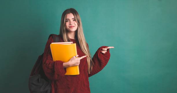 istock Happy female university student pointing to copy space and holding books 2043449253