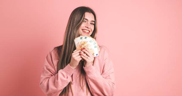 Smiling woman holding fanned out 50 euro banknotes in pink studio stock photo