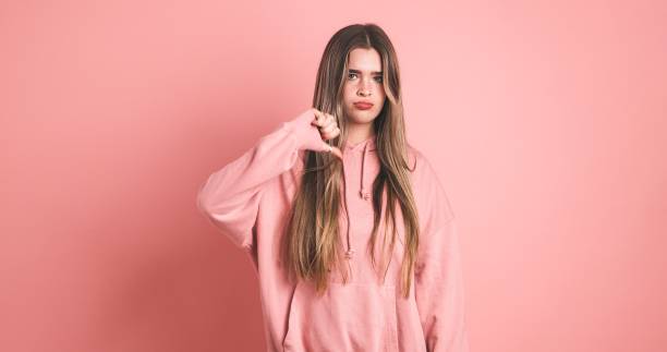 istock Disappointed female model showing thumb down sign against pink background 2043449256