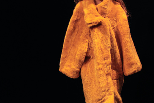 Bright yellow women's fur coat on a black background. Winter fashionable look