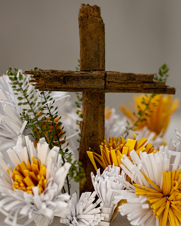 Wooden cross on natural background surrounded by white and yellow paper flowers, representation of the Easter concept, the tree of life.