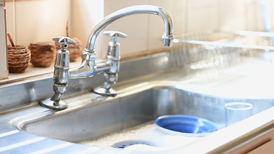 Faucet, cleaning and running water in the kitchen sink of a home for hygiene or washing dishes. Tap, flow and cleanliness with a stream of liquid in a house to clean for the removal of bacteria