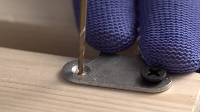A carpenter marks and drill hole in the board for a self-tapping screw to attach a furniture keyhole hanger