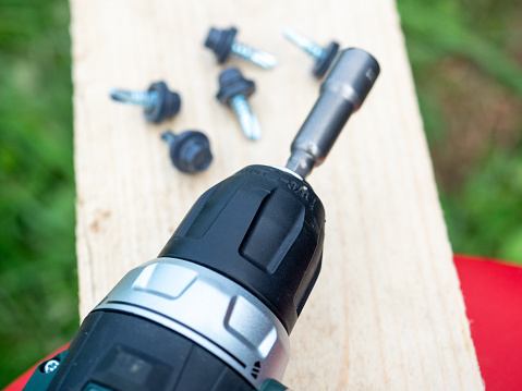 Close-up of an electric screwdriver with a special attachment for roofing screws. Construction and installation concept