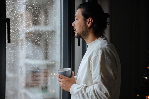 Young adult man holding coffee cup while looking away.